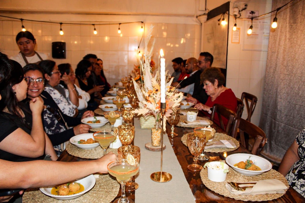 Invitados compartiendo una mesa larga con flores, velas y cristalería ámbar bajo luz cálida