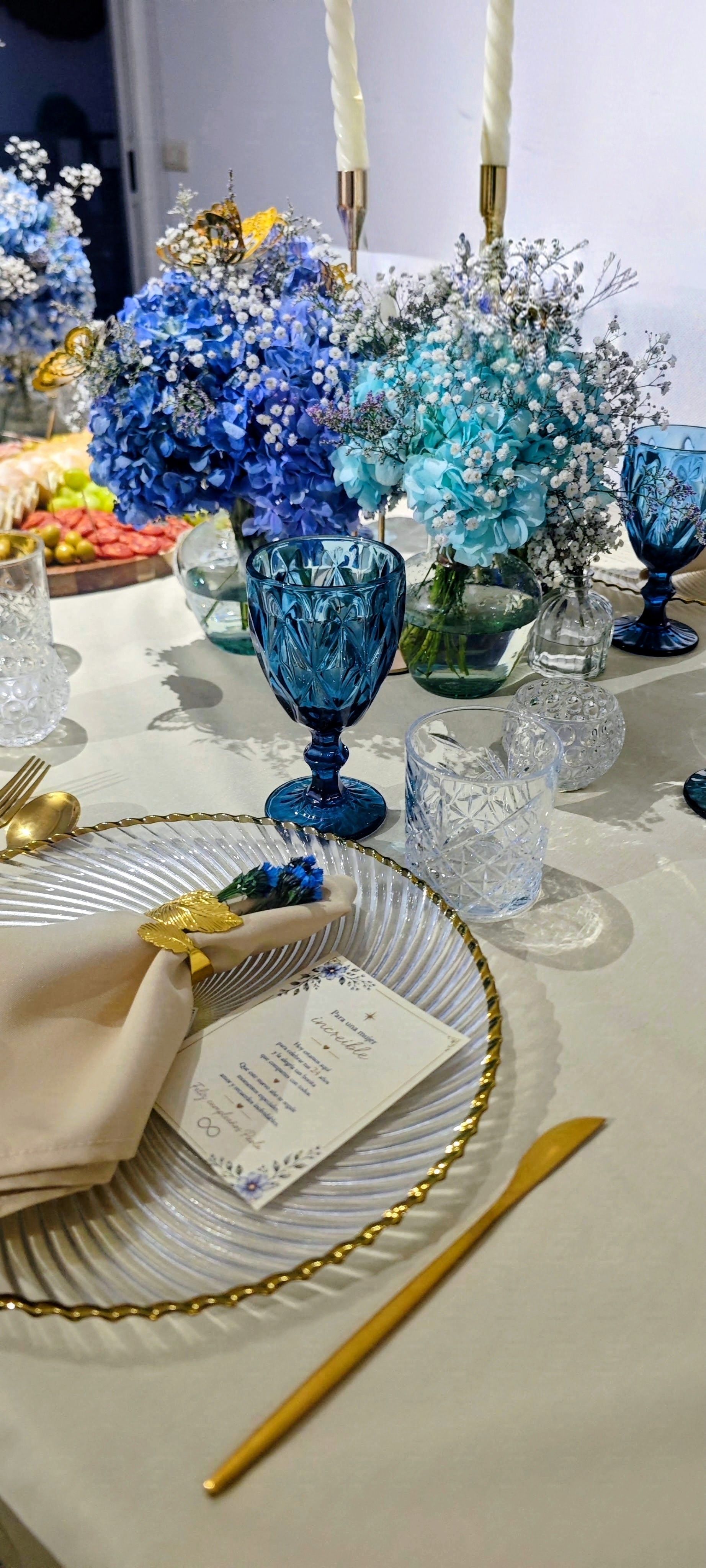Mesa con flores azules, cristalería transparente, velas y textiles claros
